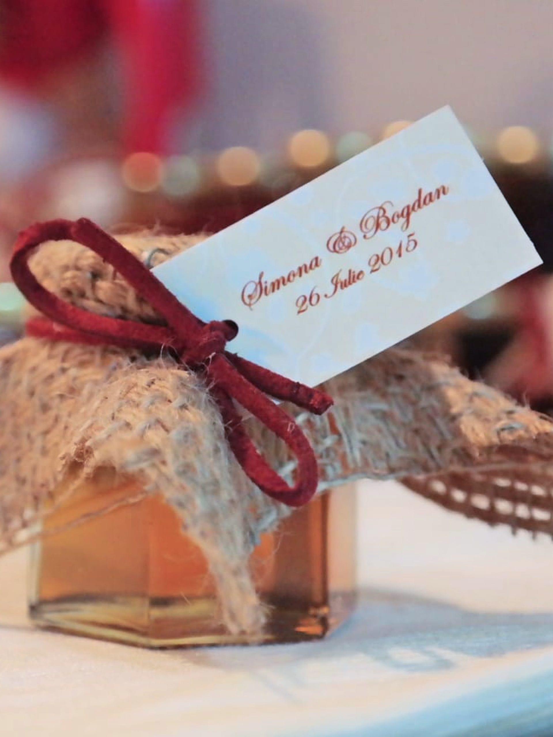 Hexagonal honey jar covered with burlap and tied with a burgundy cord, with a personalized tag, as a wedding favor